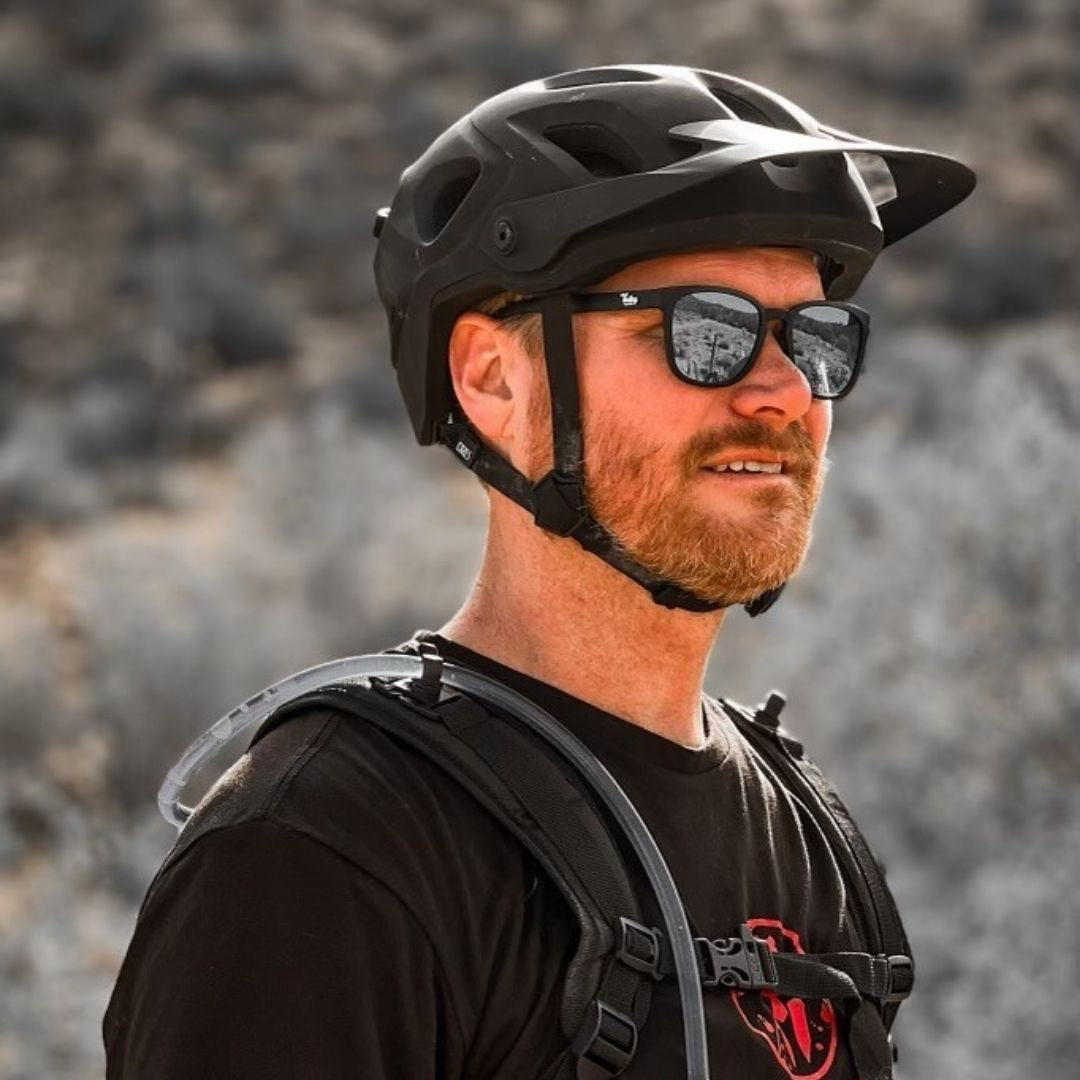 Man wearing a black helmet and sunglasses with a blurred natural background